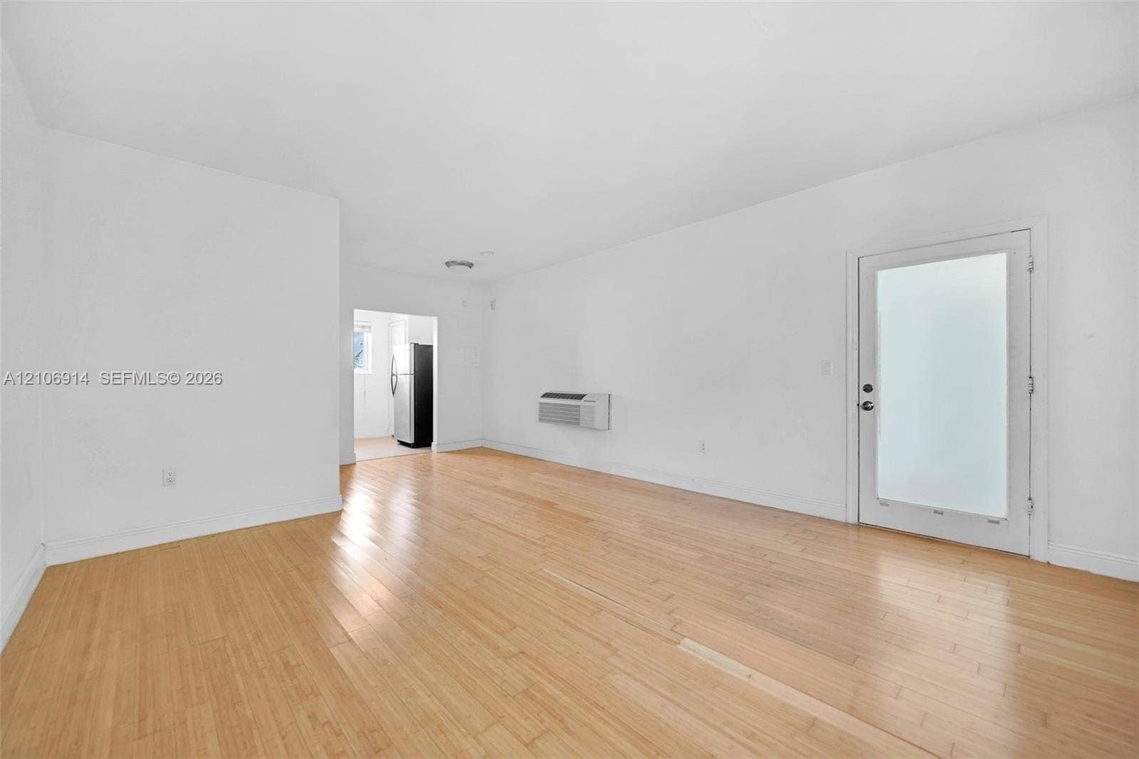 320 85th Street, #20, Miami Beach, Miami Beach, FL 33141 Open interior space featuring light wood-finish flooring, a wall-mounted climate control unit, and an exterior door with frosted glass paneling