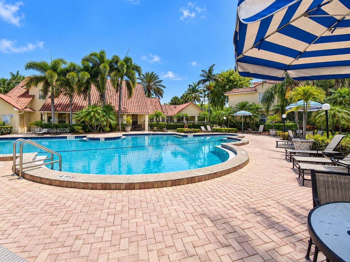 Swimming pool featuring a curved concrete perimeter, metal handrails, and surrounding brick-paver patio with mature palm trees