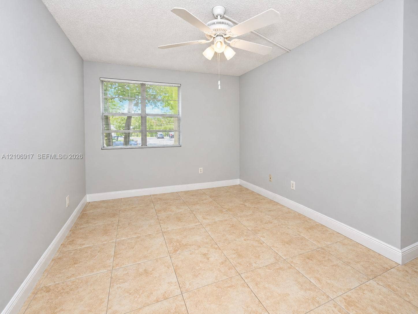 Neutral-toned interior space featuring tile flooring, a dual-pane window, and a ceiling fan with integrated lighting