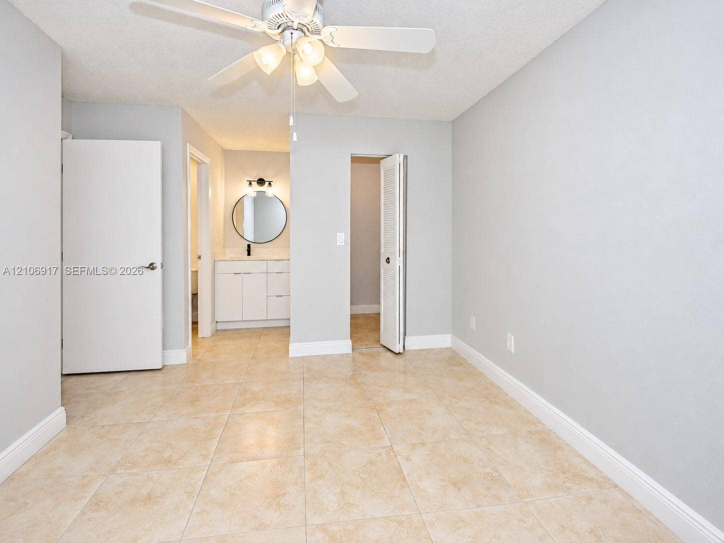 Neutral wall tones with tile flooring, a multi-blade ceiling fan with integrated lighting, and a white vanity cabinet featuring a circular mirror and matte black hardware