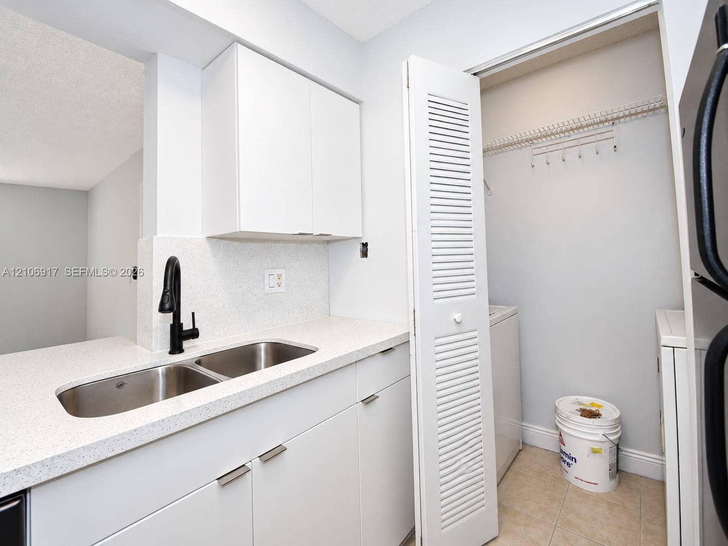 Utility space featuring white cabinetry, stone-finish countertops, a double-basin stainless steel sink with a matte black high-arch faucet, and a louvered bi-fold door closet with built-in shelving
