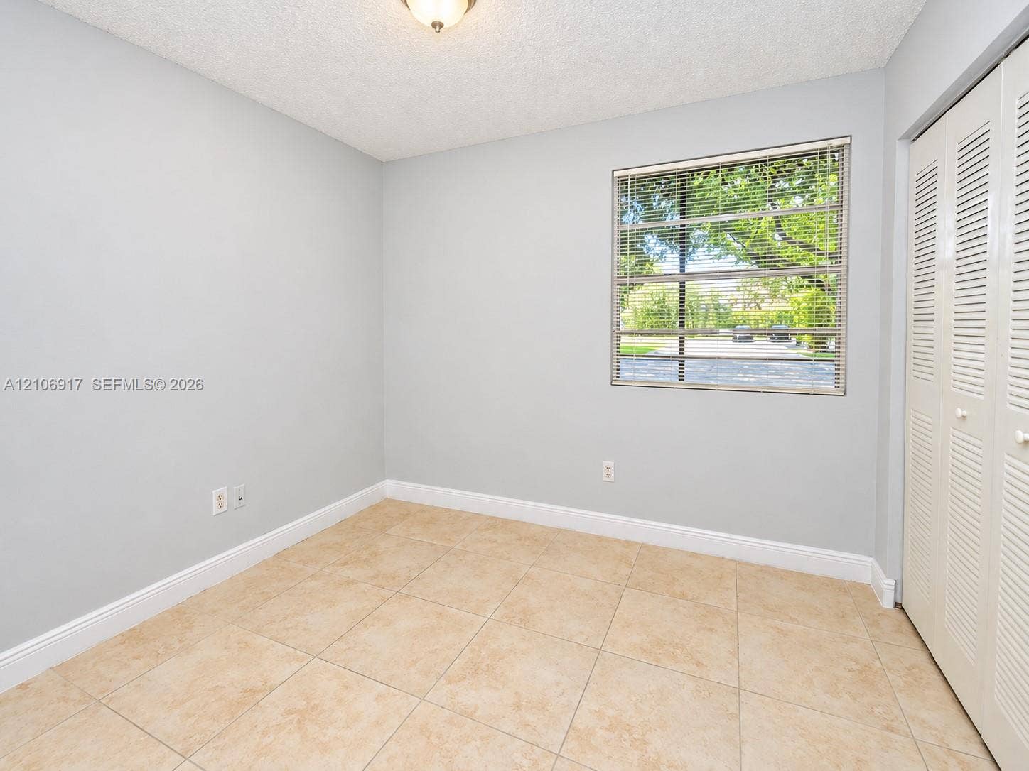 2nd bedroom- Neutral-toned interior featuring large-format ceramic tile flooring, a window with horizontal blinds, and built-in bi-fold closet doors