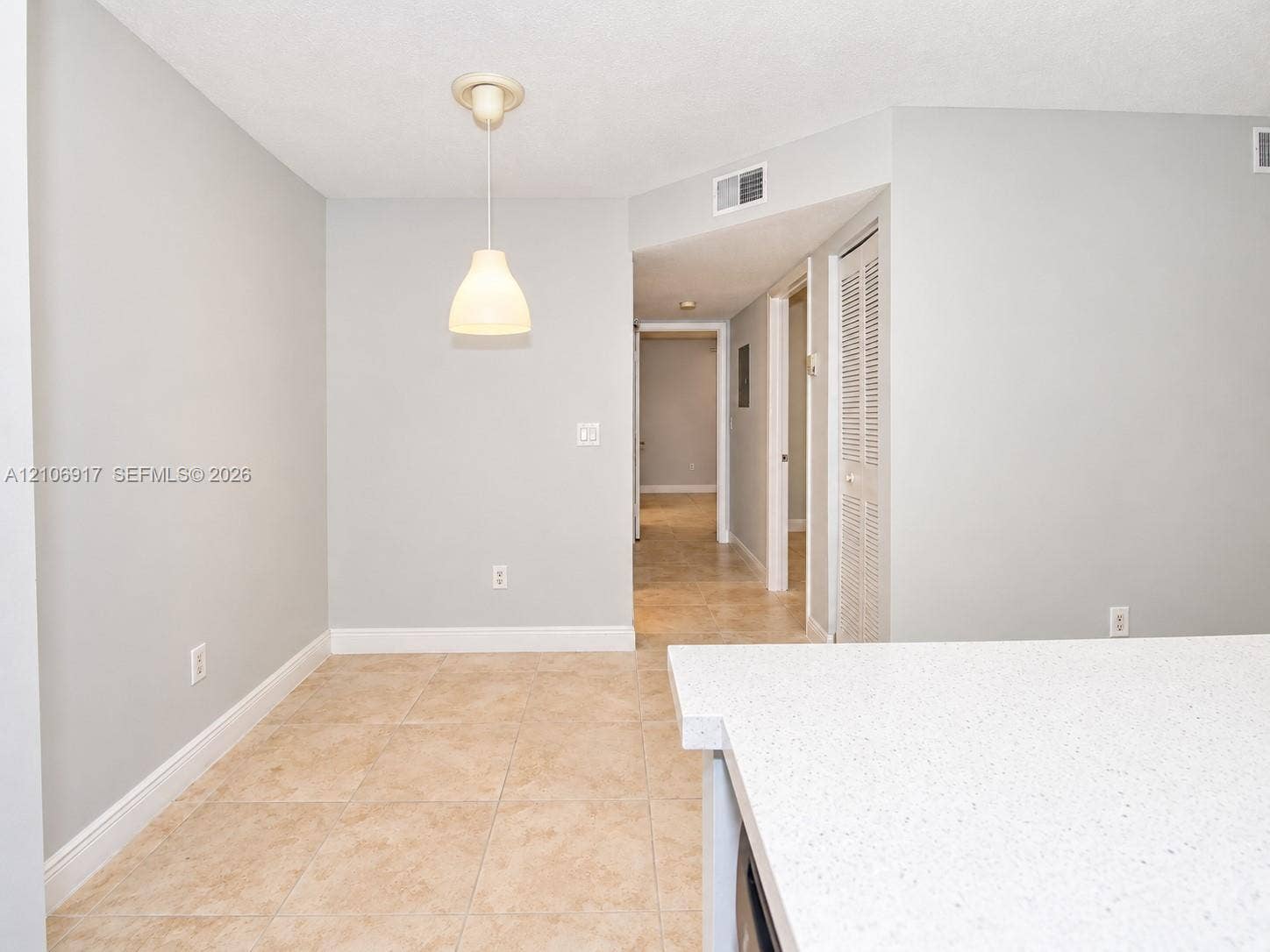 Neutral-toned interior featuring ceramic tile flooring, a hanging pendant light, and a stone-surface countertop