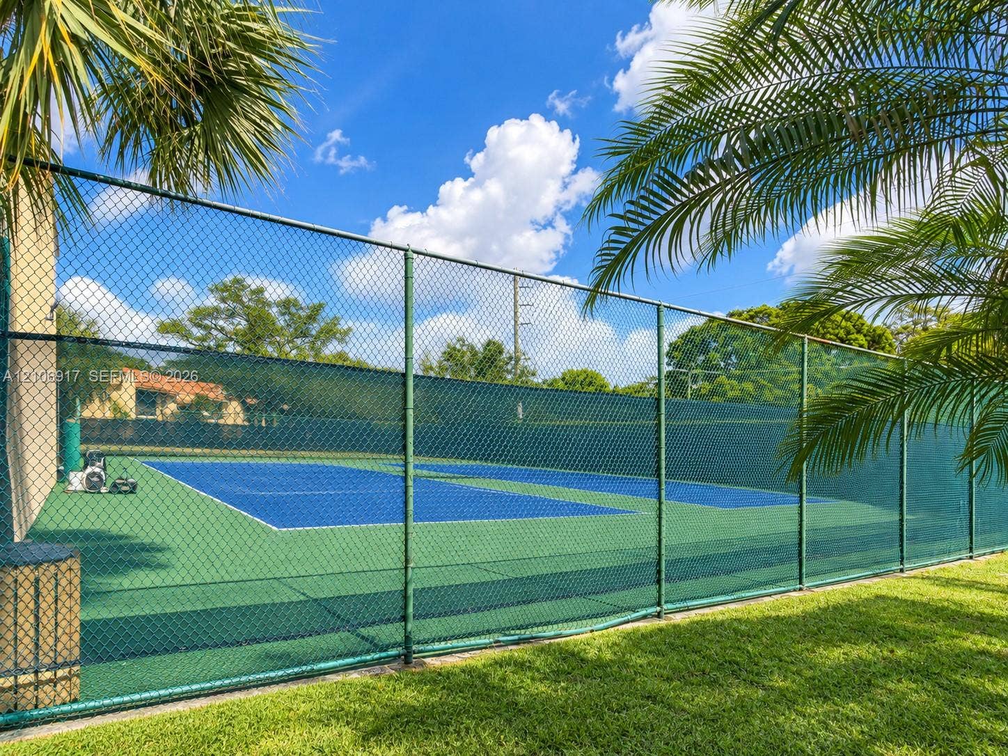 Private tennis court featuring a hard surface, perimeter chain-link fencing, and mature palm landscaping
