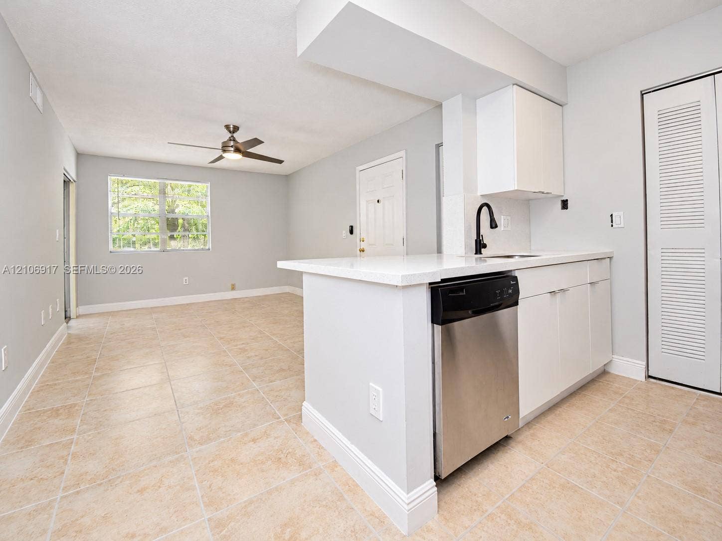 Kitchen featuring white cabinetry, solid-surface countertops, a stainless steel dishwasher, and a matte black gooseneck faucet, set against tile flooring throughout the open-concept space and a ceiling fan