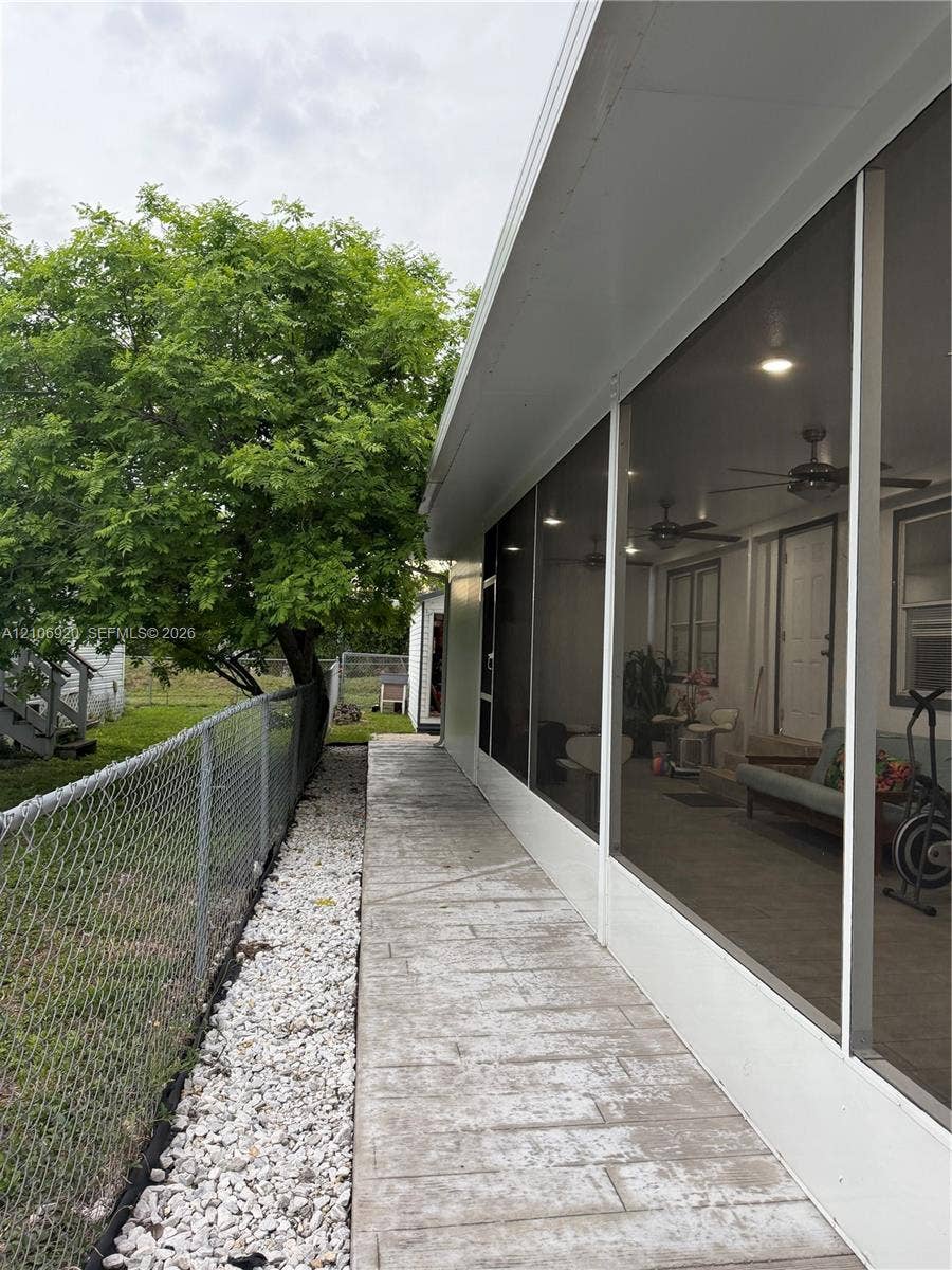 19800 SW 180 Avenue, #t, Miami, FL 33187 Screened-in porch featuring a textured concrete floor, multiple ceiling fans, and recessed lighting, accompanied by a side yard with gravel ground cover and chain-link perimeter fencing