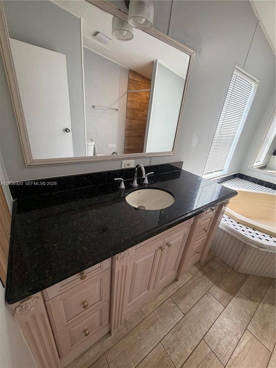 19800 SW 180 Avenue, #t, Miami, FL 33187 Vanity with a dark stone countertop, integrated sink, wood-finish cabinetry, a large framed mirror, and wood-finish flooring