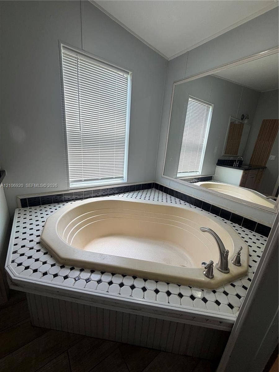 19800 SW 180 Avenue, #t, Miami, FL 33187 Oversized soaking tub featuring a tiled surround in a black and white geometric pattern, integrated deck-mounted faucet, and a large wall-mounted mirror