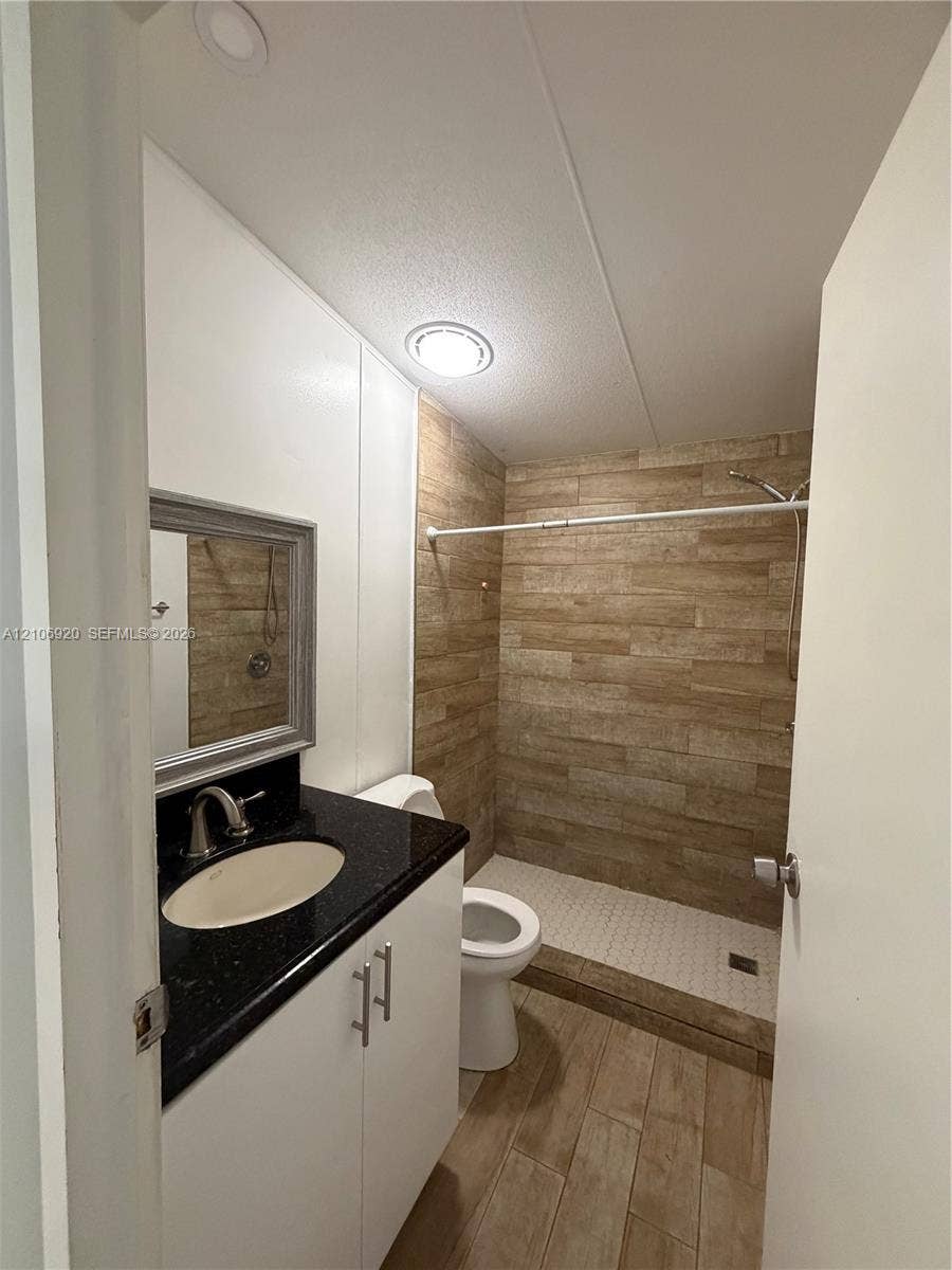19800 SW 180 Avenue, #t, Miami, FL 33187 Bathroom featuring a vanity with a dark stone countertop, an integrated oval sink, wood-finish flooring, and a walk-in shower with tile surround