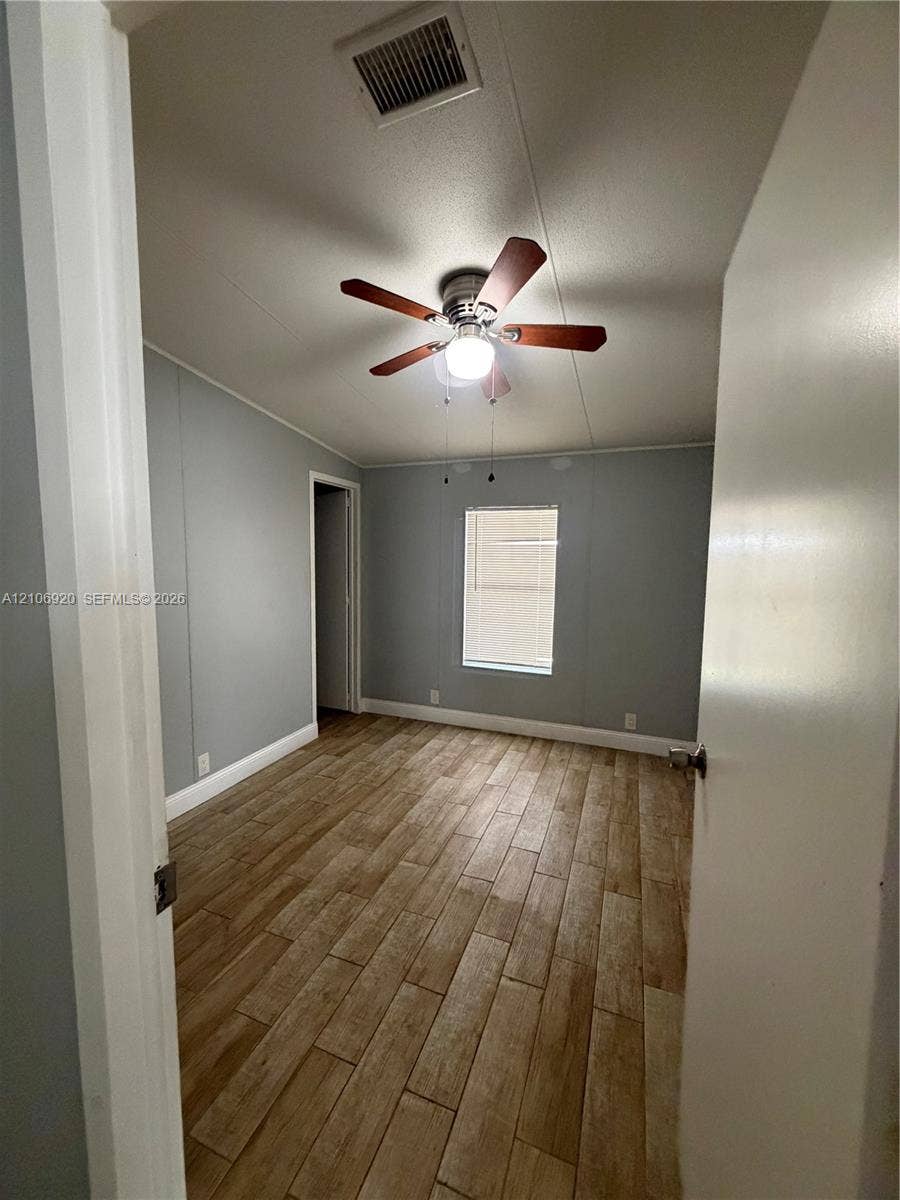 19800 SW 180 Avenue, #t, Miami, FL 33187 Room featuring wood-finish flooring, neutral wall tones, a single-pane window, and a ceiling fan with integrated lighting