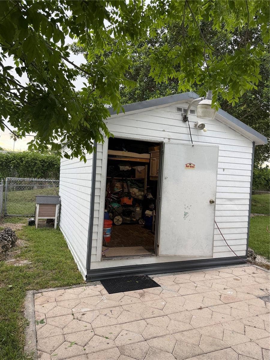 19800 SW 180 Avenue, #t, Miami, FL 33187 Detached storage shed featuring white horizontal siding, a gable roof, an exterior utility light, and concrete paver hardscaping