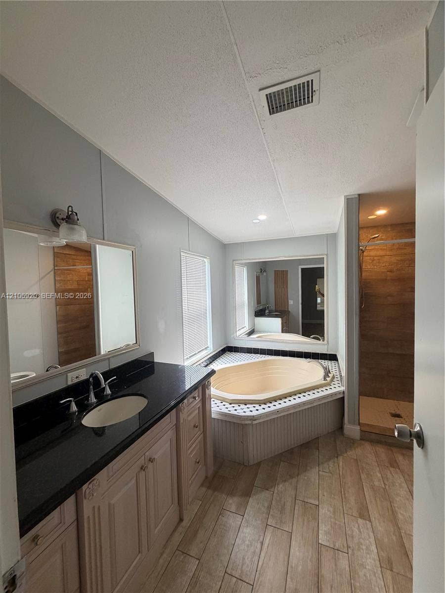 19800 SW 180 Avenue, #t, Miami, FL 33187 Bathroom featuring wood-finish flooring, a vanity with a dark countertop and integrated sink, a deep soaking tub with a tiled surround, and a walk-in shower with wood-patterned wall tile
