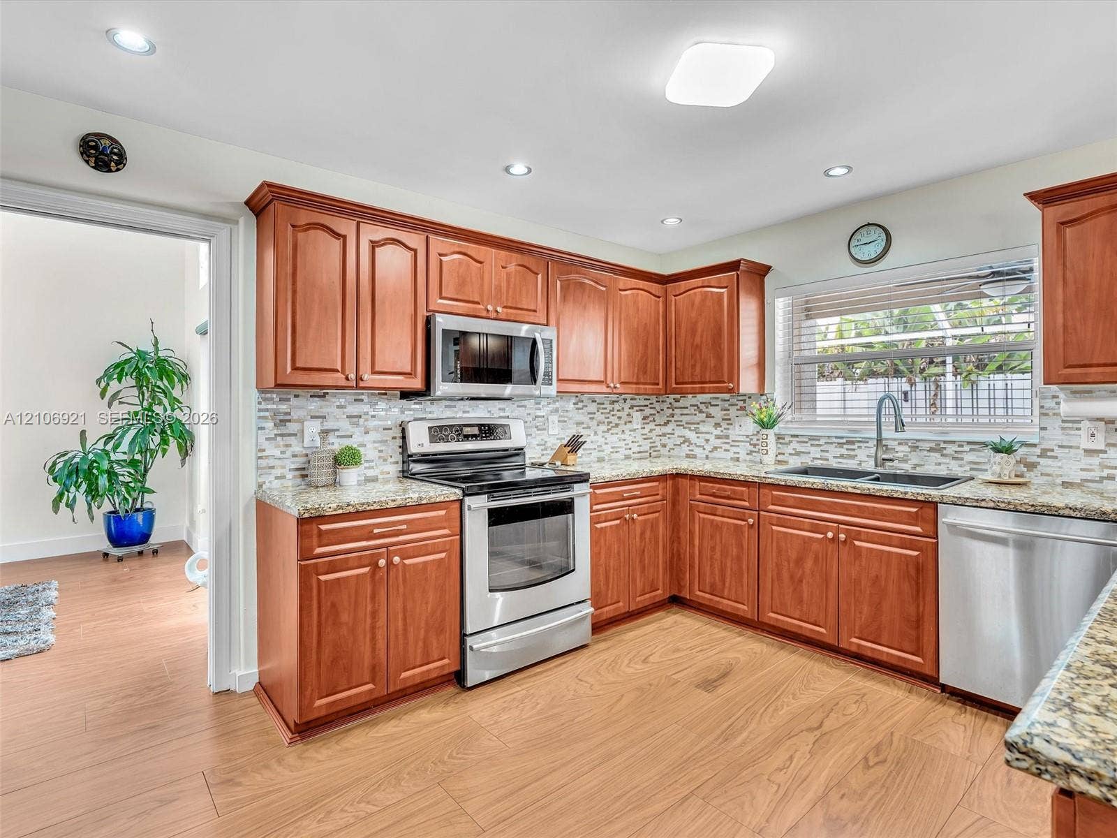 Kitchen featuring wood cabinetry, stone-finish countertops, decorative tile backsplash, wood-finish flooring, and stainless steel appliances