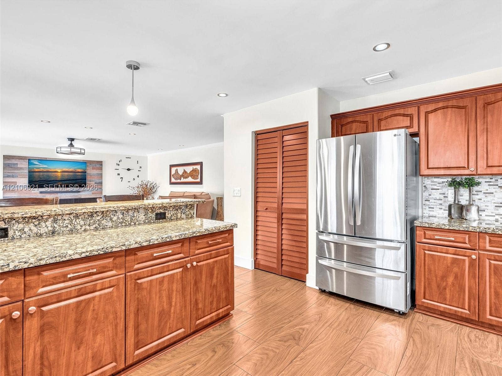Kitchen featuring wood cabinetry, stone countertops, stainless steel refrigerator, tile backsplash, and wood-finish flooring