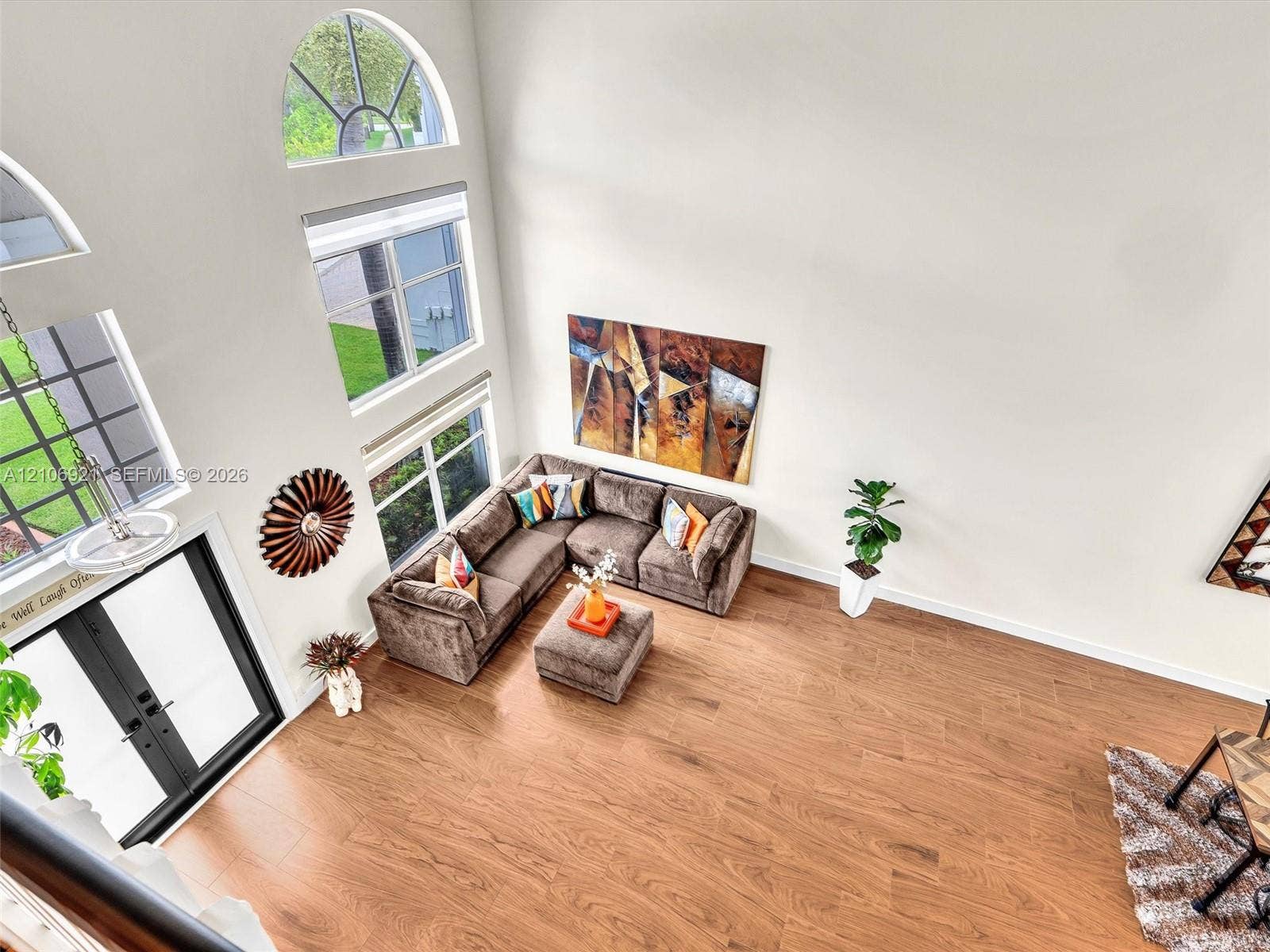 High-ceilinged room featuring wood-finish flooring, a multi-pane arched window, and a modern dual-pane window configuration with a hanging pendant light fixture