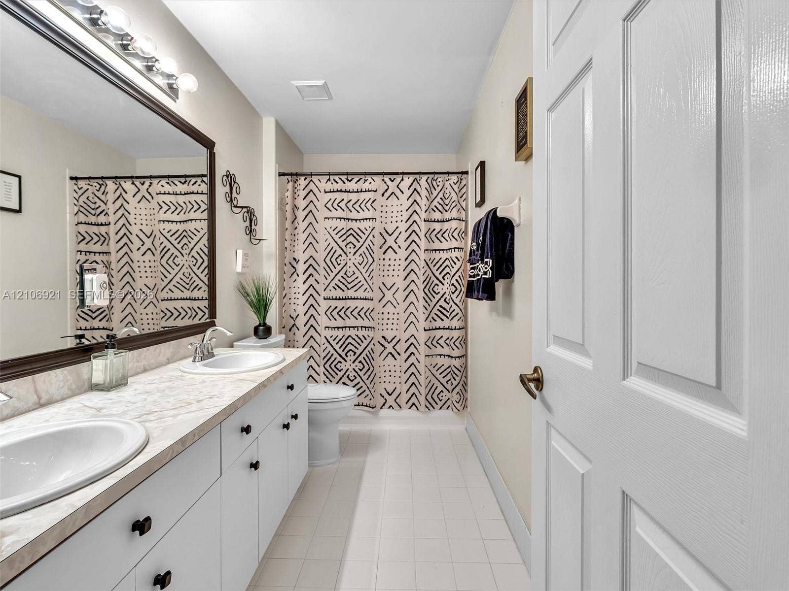 Bathroom featuring a dual-sink vanity with a stone-finish countertop, white cabinetry with dark hardware, a full-width mirror, and a tub-shower combination