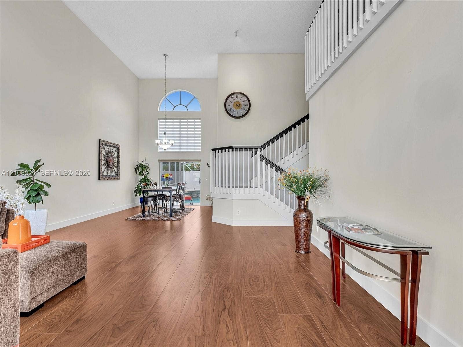 High-ceilinged interior featuring wood-finish flooring, a staircase with a white balustrade and dark wood handrail, and an arched window