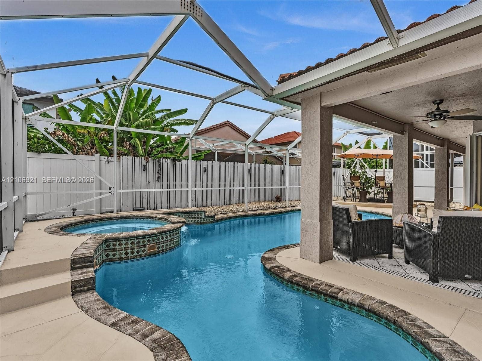 Screened-in outdoor living area featuring a custom swimming pool with spillover spa, decorative tile accents, stone-finished coping, and a covered lanai