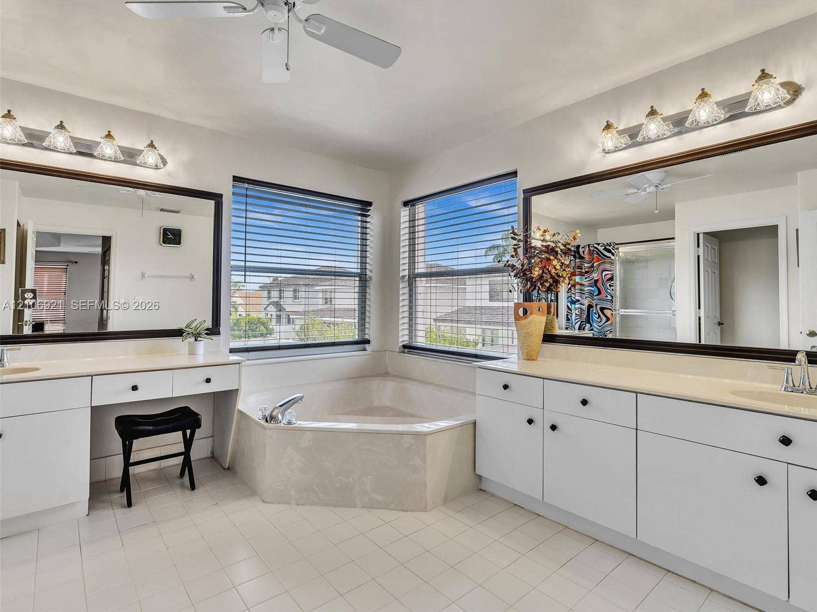 Dual white vanities with integrated sinks, corner soaking tub, large wall-mounted mirrors, and multi-light fixtures