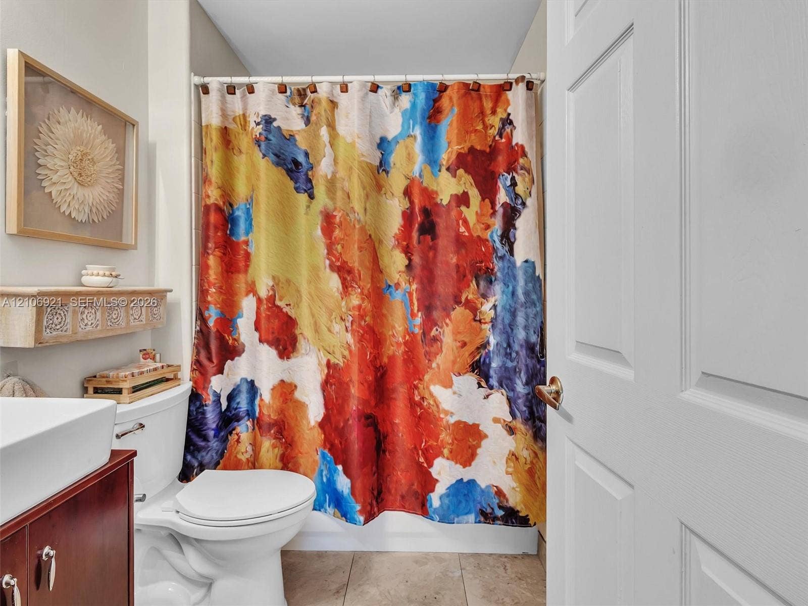 Bathroom featuring a wood-tone vanity, white ceramic sink, wall-mounted decorative shelving, and tile flooring