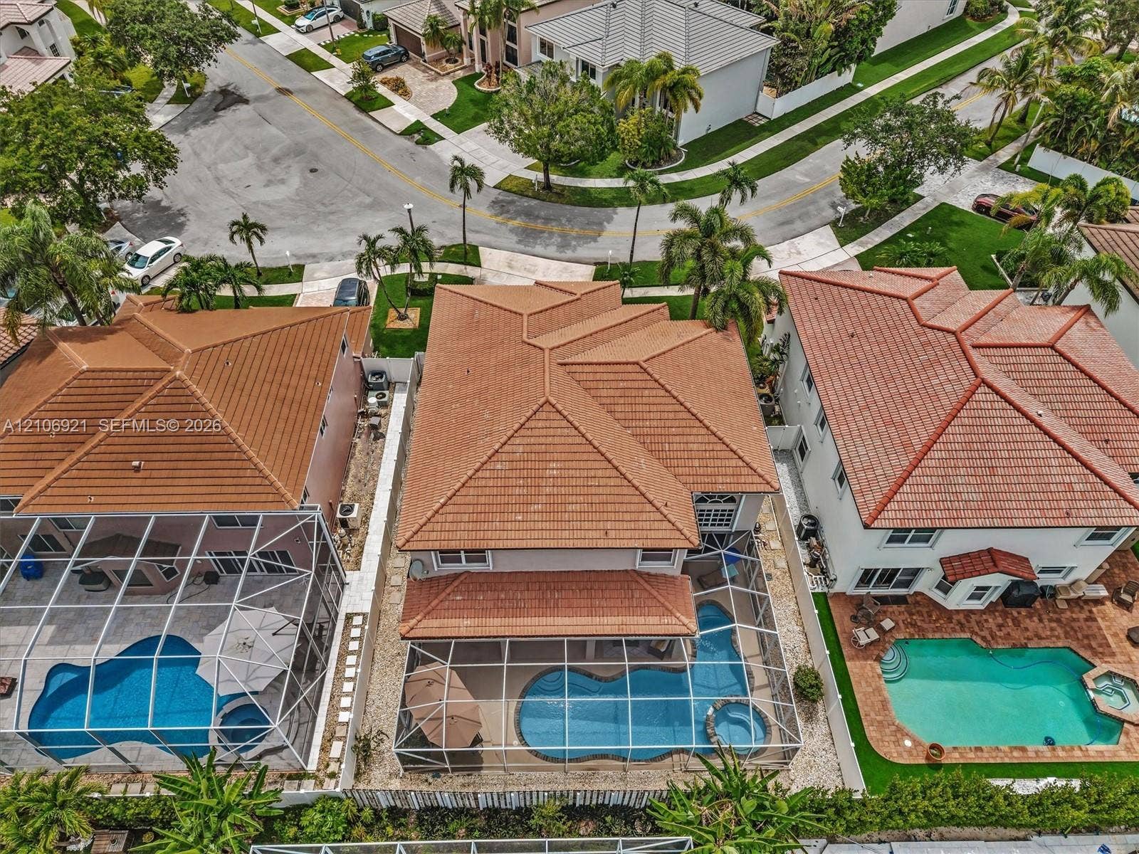 Multi-level residence featuring a terracotta-tiled hip roof and a screened-in rear patio enclosure containing an in-ground swimming pool and integrated spa