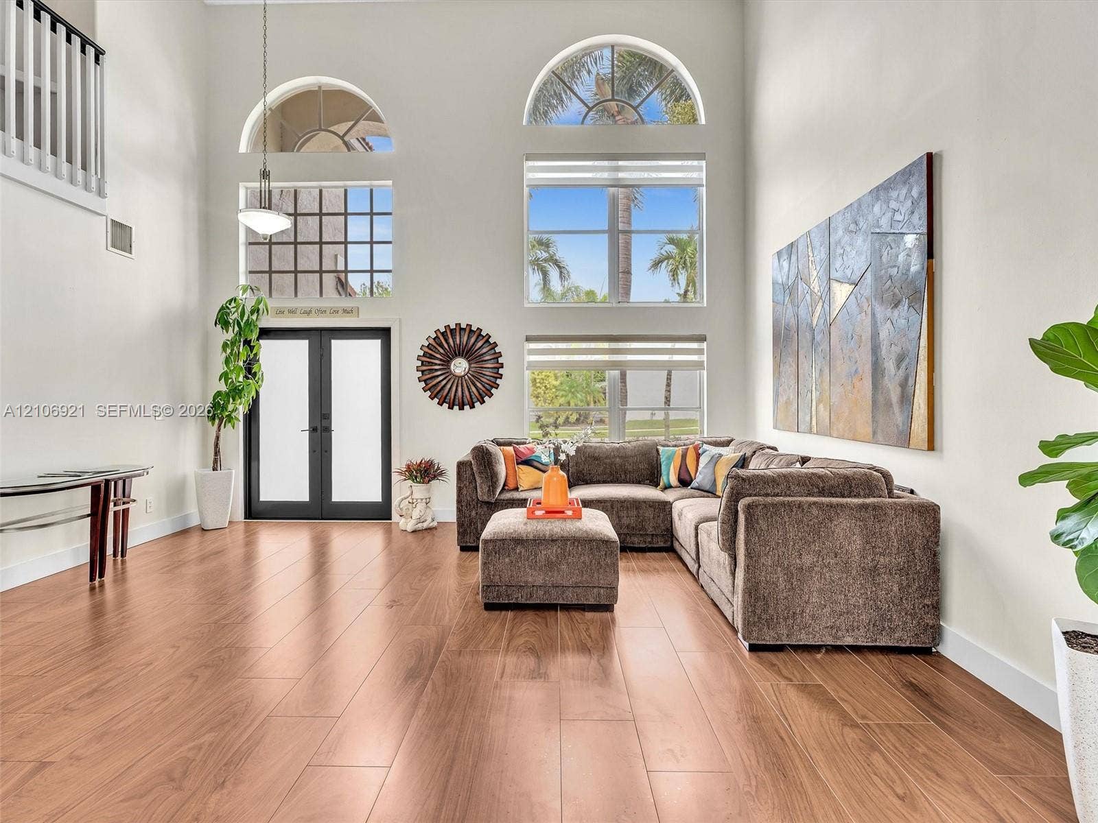 Expansive living space featuring soaring ceilings, wood-finish flooring, floor-to-ceiling windows with arched transoms, and a black-framed glass entry door