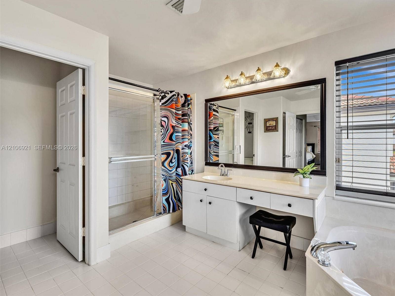 Bathroom featuring a vanity with integrated cabinetry, a large framed mirror, a built-in soaking tub, a walk-in shower with glass enclosure, and tiled flooring