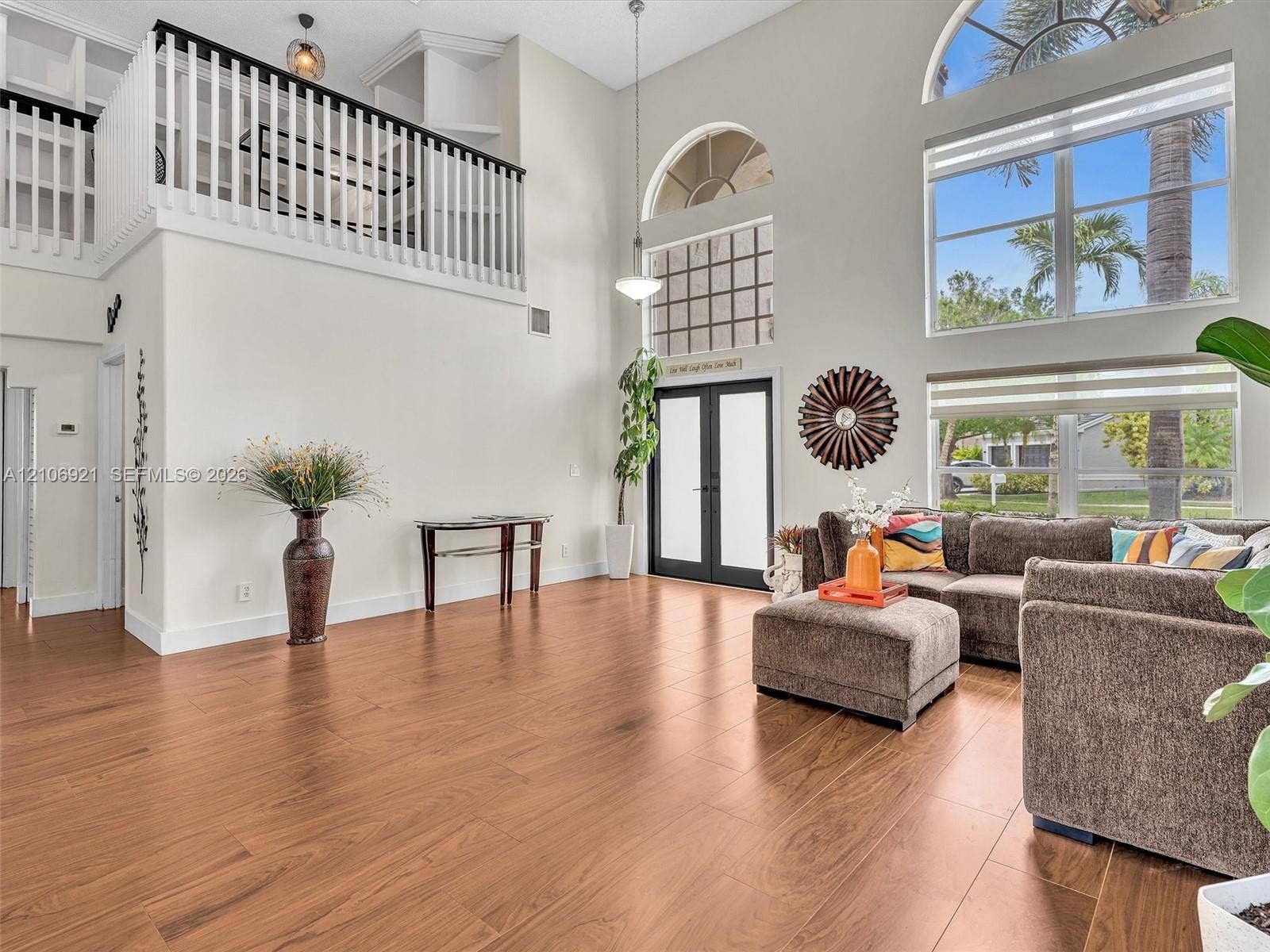 Double-height ceiling, arched windows, wood-finish flooring, and white railing balcony overlooking the space
