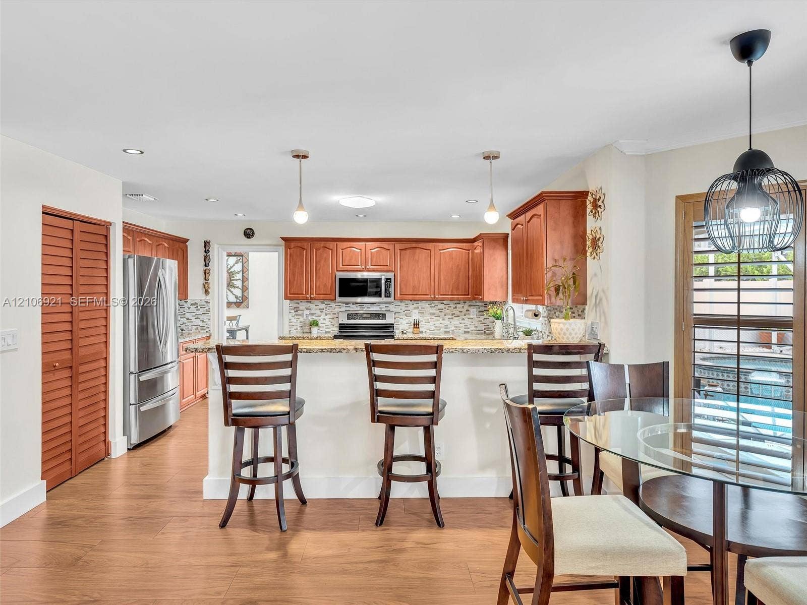 Kitchen featuring wood cabinetry, stone countertops, stainless steel appliances, decorative tile backsplash, and wood-finish flooring