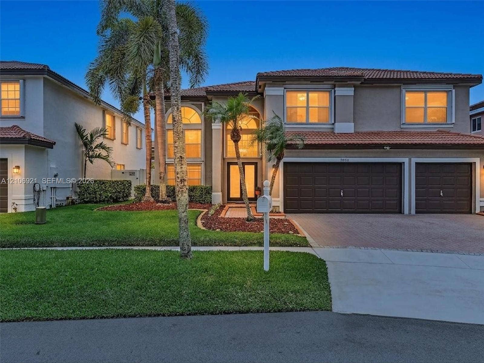 Two-story stucco exterior featuring a tile roof, multi-car garage with paneled doors, expansive arched windows, and a paved driveway