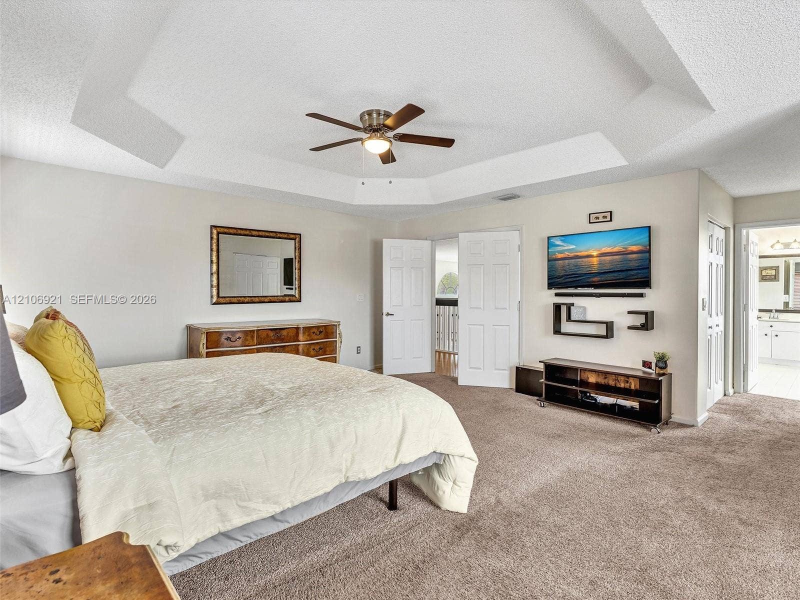 Tray ceiling with an integrated light-and-fan fixture, neutral wall finishes, and carpeting