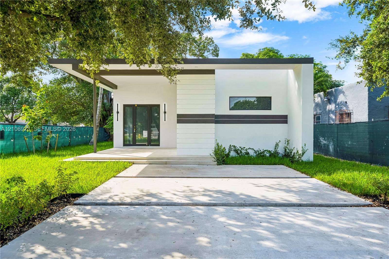 870 Superior Street, Opa Locka, FL 33054 Modern exterior featuring smooth white stucco finish, flat roofline with dark trim, expansive concrete driveway, covered porch, and vertical wall-mounted lighting fixtures