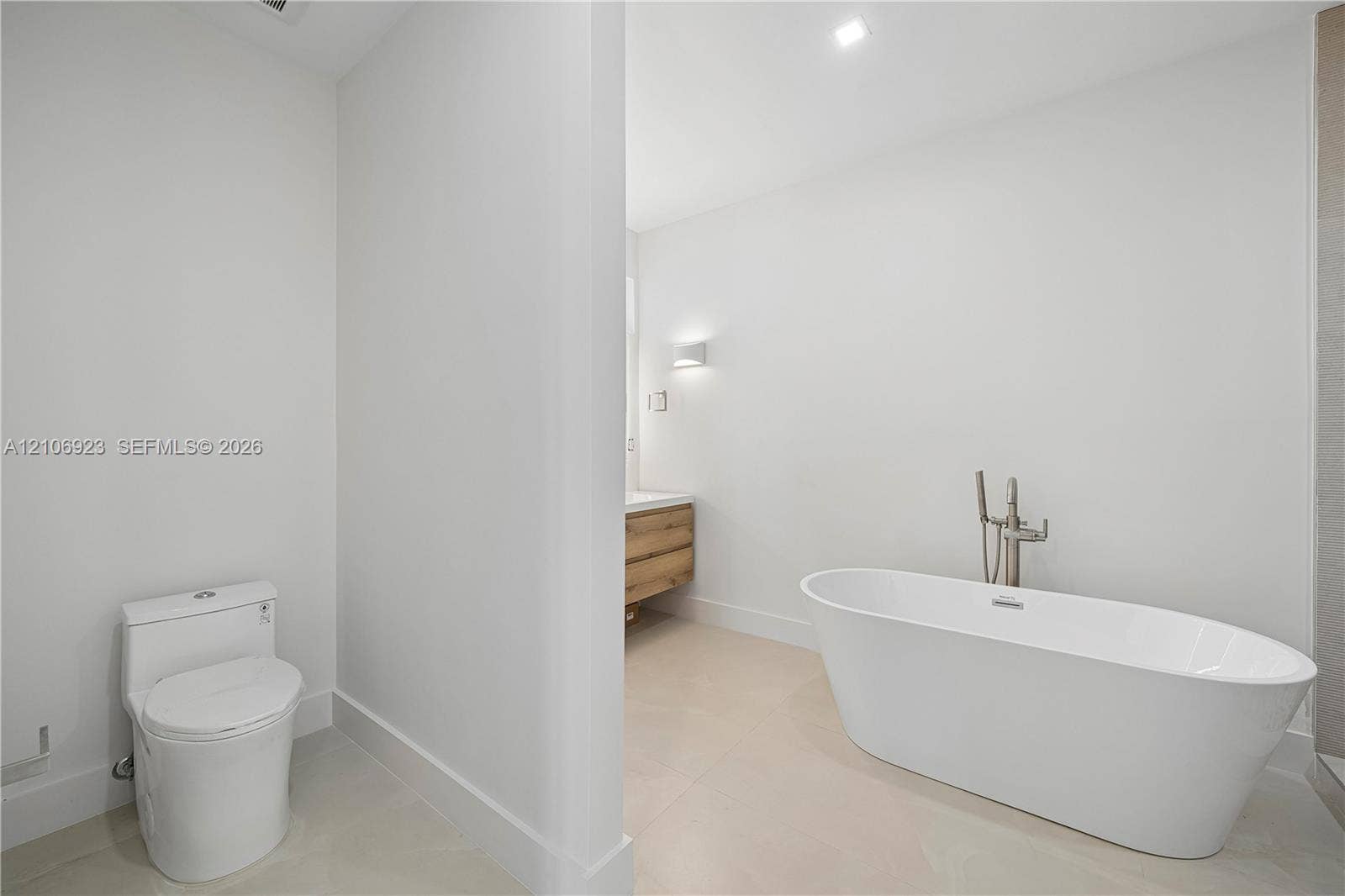 870 Superior Street, Opa Locka, FL 33054 Freestanding white soaking tub with polished chrome floor-mounted faucet, wood-finish vanity with countertop basin, and low-profile elongated toilet