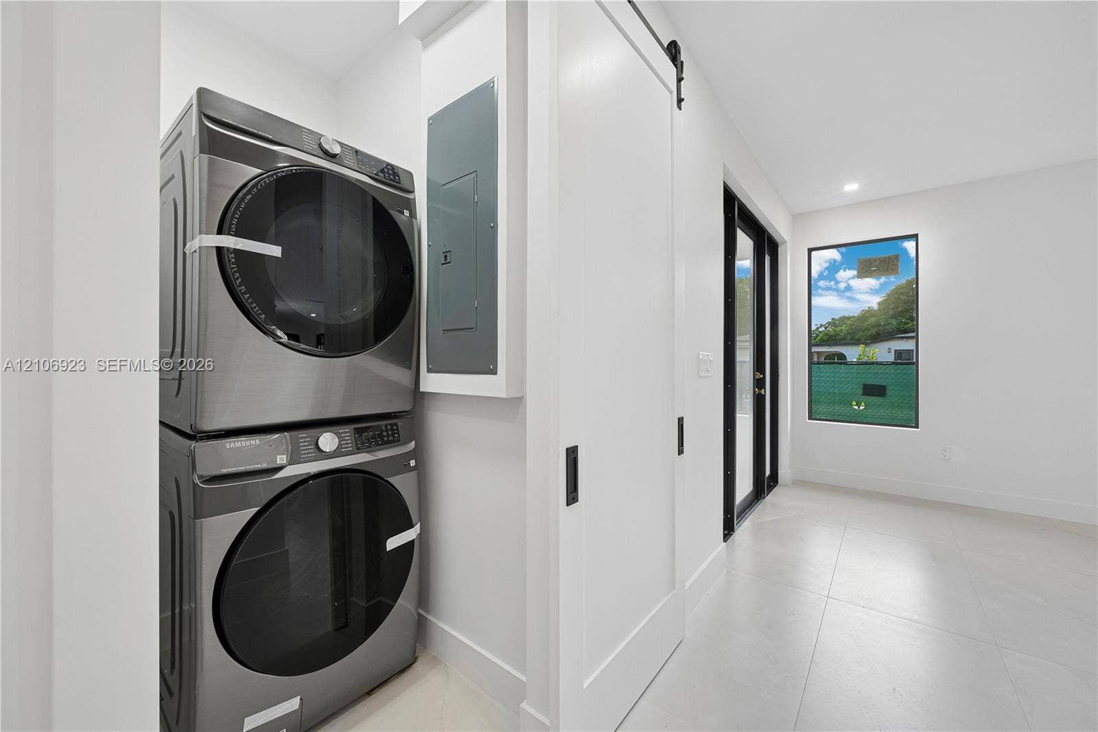 870 Superior Street, Opa Locka, FL 33054 Laundry space featuring large-format tile flooring, a white sliding barn door with matte black hardware, and an exterior glass door with a black frame