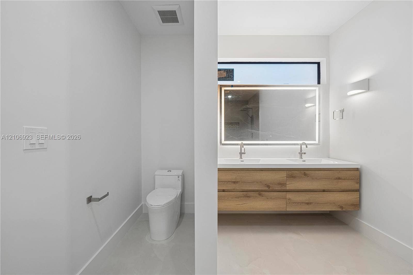 870 Superior Street, Opa Locka, FL 33054 Dual-sink floating vanity with wood-finish cabinetry, rectangular vessel sinks, wall-mounted faucets, and an integrated LED-backlit mirror featuring a horizontal clerestory window