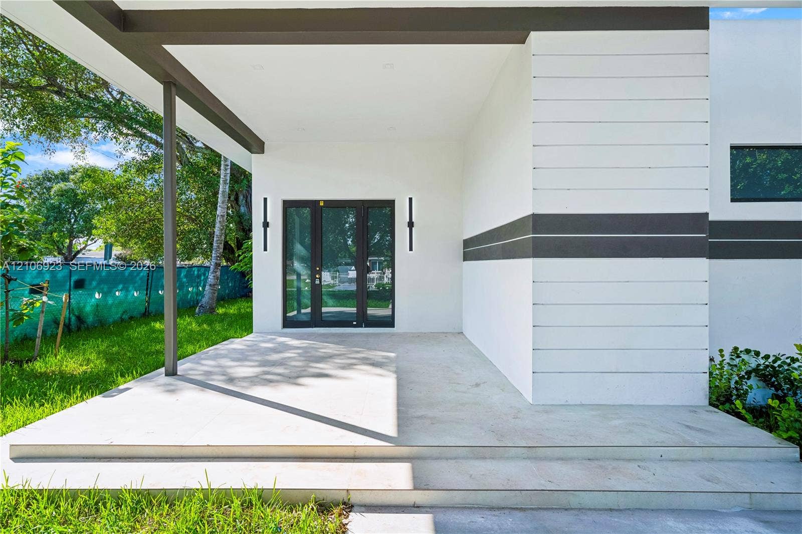870 Superior Street, Opa Locka, FL 33054 Modern entrance featuring horizontal wood-panel siding, a covered concrete porch, tiered stairs, and dual vertical wall-mounted exterior light fixtures