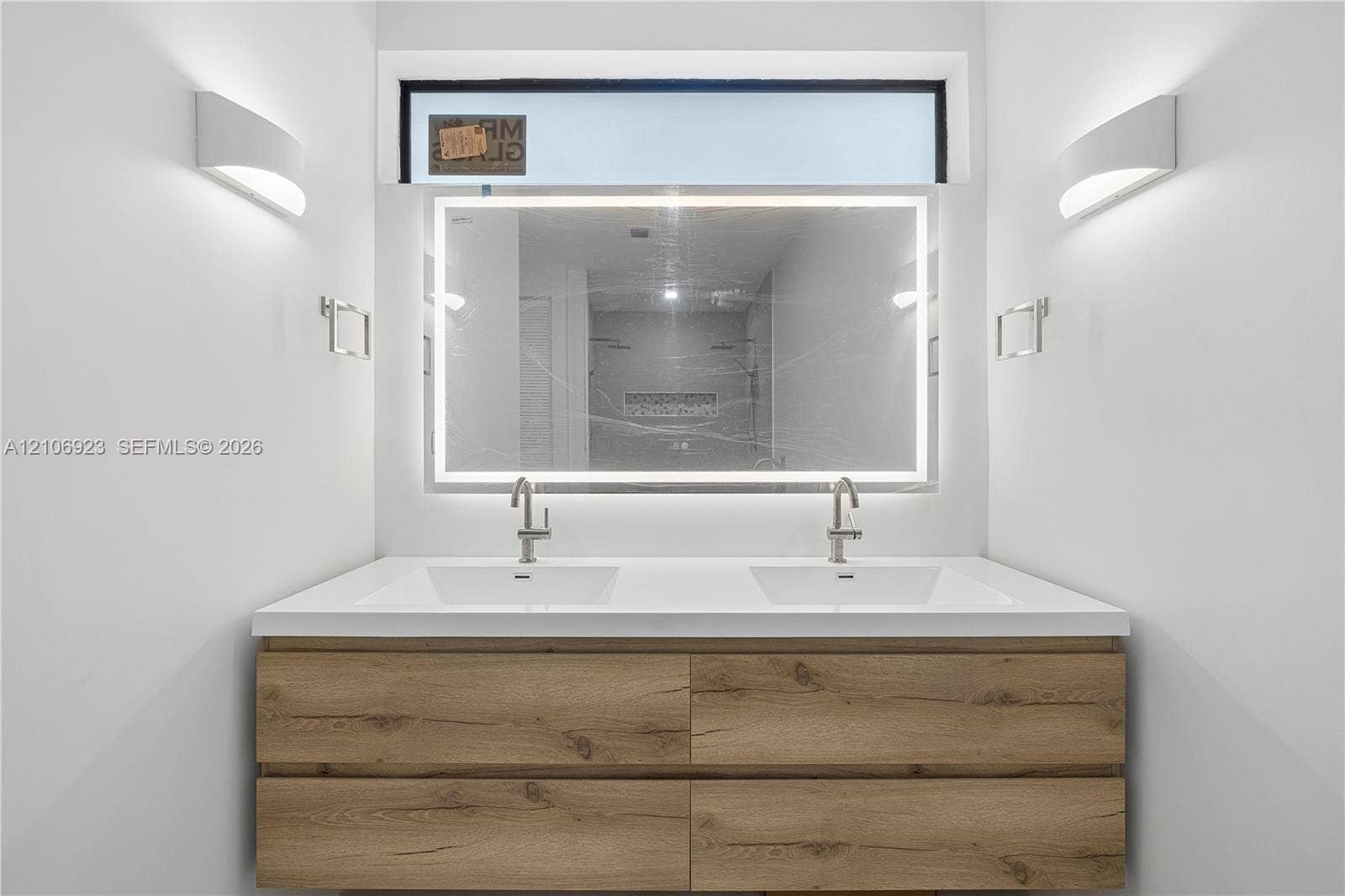 870 Superior Street, Opa Locka, FL 33054 Double vanity with wood-finish cabinetry, solid surface countertop, integrated dual sinks, LED-backlit mirror, and wall-mounted sconces