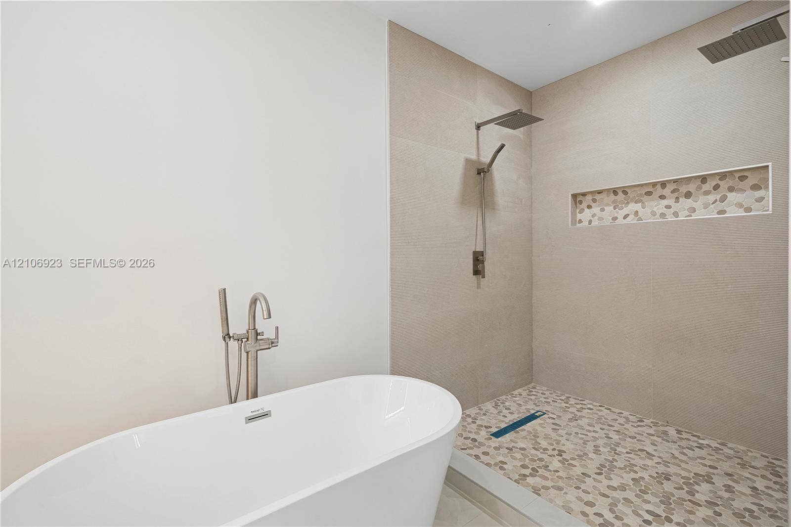 870 Superior Street, Opa Locka, FL 33054 Freestanding soaking tub with a floor-mounted brushed nickel faucet, walk-in shower featuring large-format wall tile, pebble-stone flooring, rainfall showerhead, and a built-in tiled shower niche