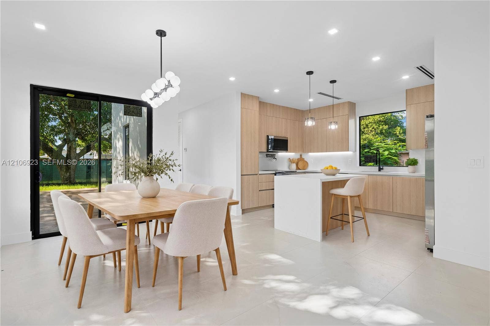 870 Superior Street, Opa Locka, FL 33054 Modern kitchen featuring flat-panel wood cabinetry, a waterfall-edge center island with quartz countertops, recessed lighting, and large sliding glass doors providing outdoor access