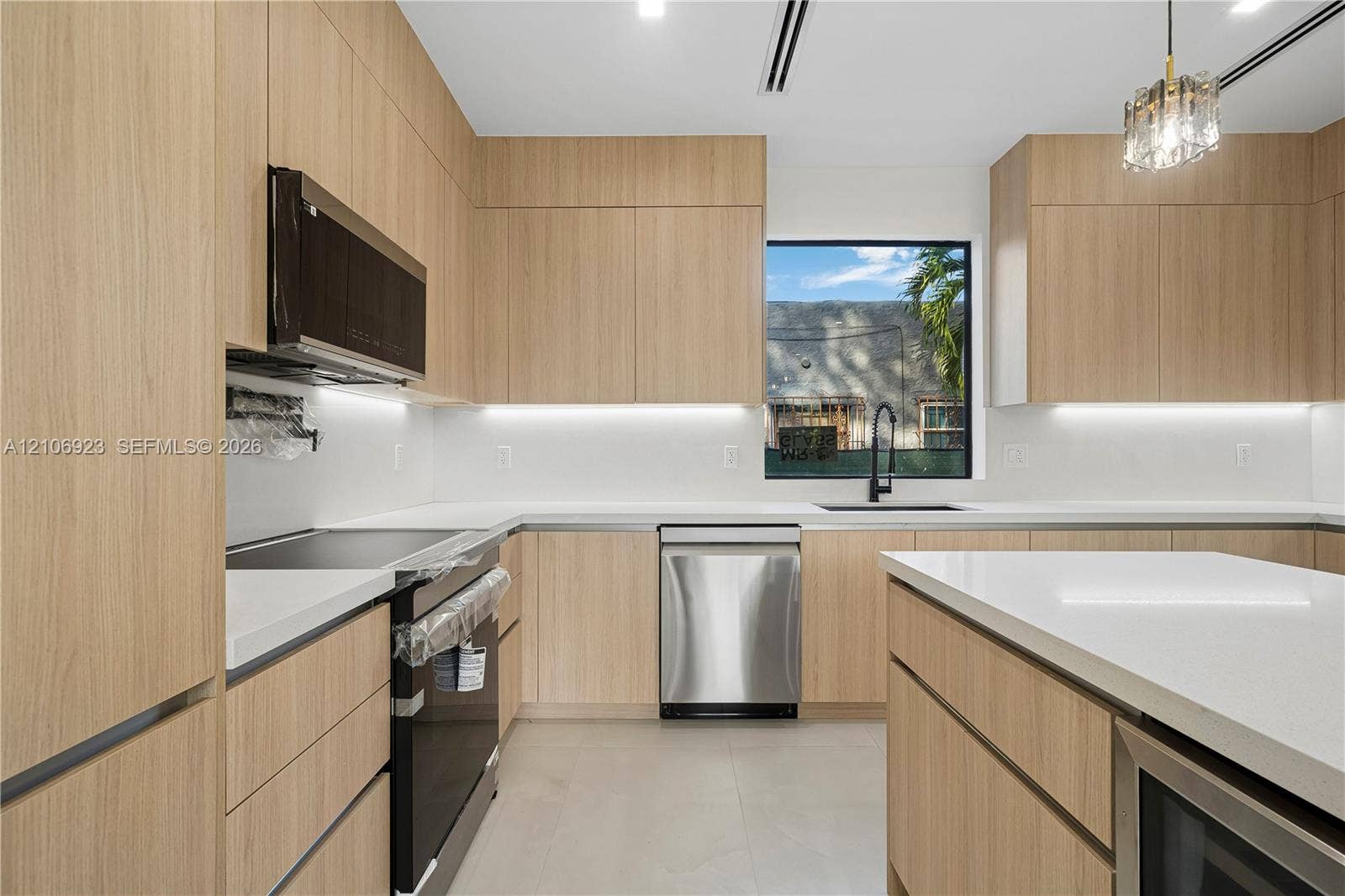 870 Superior Street, Opa Locka, FL 33054 Kitchen featuring flat-panel wood-finish cabinetry, white solid-surface countertops, an integrated center island, stainless steel appliances, and under-cabinet lighting