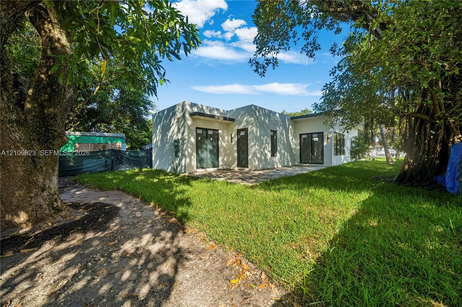 870 Superior Street, Opa Locka, FL 33054 Stucco exterior residence featuring a flat roofline, glass sliding doors, dark-frame windows, and an expansive grass yard with mature trees