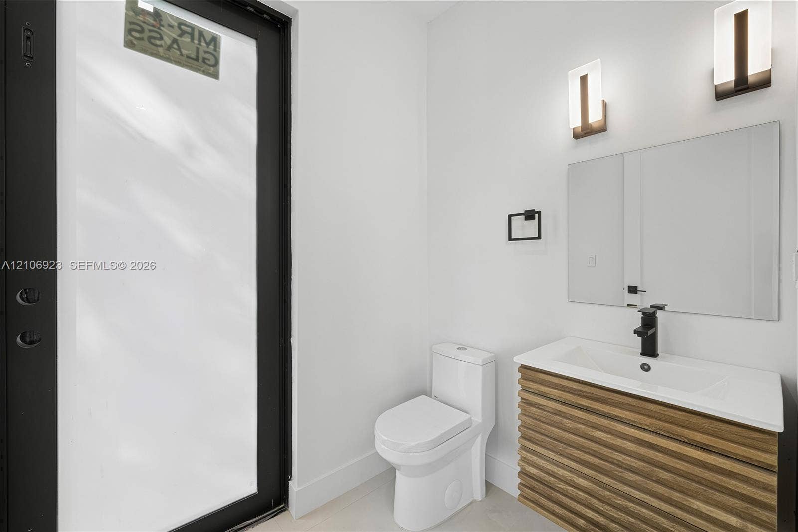 870 Superior Street, Opa Locka, FL 33054 Floating vanity featuring wood-finish reeded detailing, white integrated countertop, matte black faucet, wall-mounted rectangular mirror, and dual vertical sconces