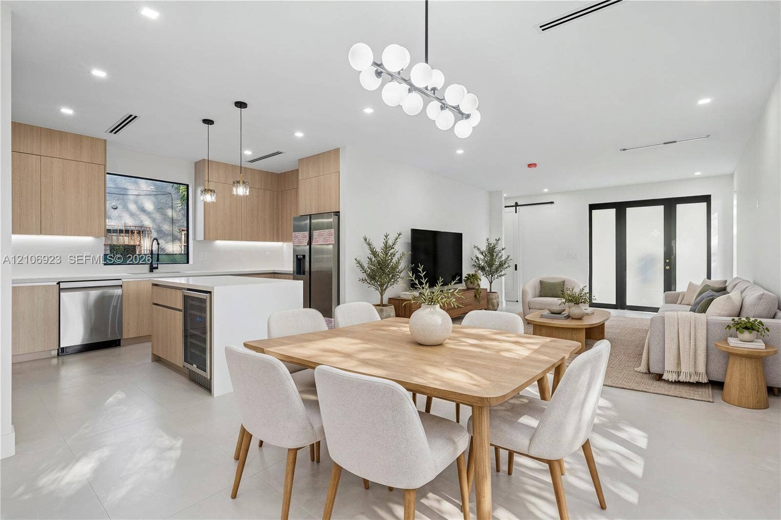 870 Superior Street, Opa Locka, FL 33054 Open-concept kitchen featuring light wood-finish cabinetry, a central island with an integrated beverage cooler, stainless steel appliances, and a modern multi-globe chandelier