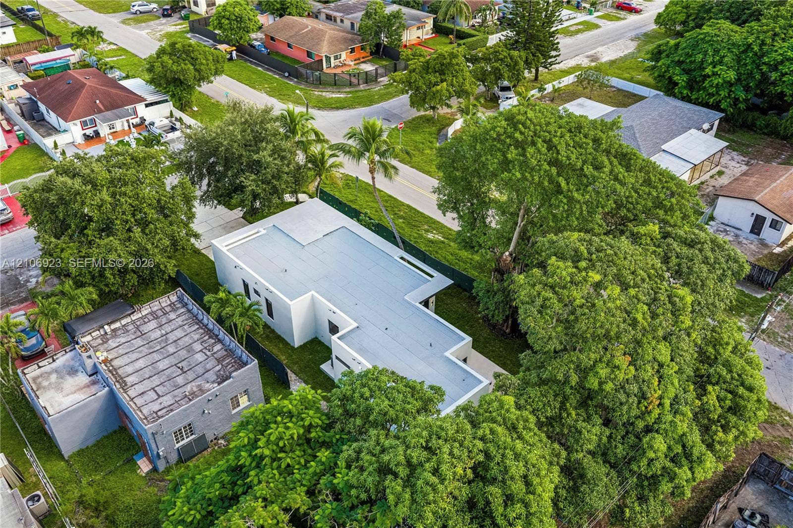870 Superior Street, Opa Locka, FL 33054 Aerial view of a rectangular property featuring a flat roof structure, concrete driveway, mature trees, and perimeter fencing
