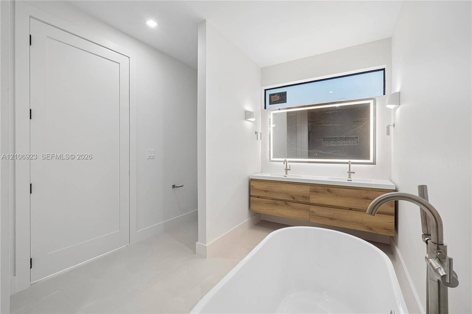 870 Superior Street, Opa Locka, FL 33054 Freestanding soaking tub with floor-mounted brushed nickel faucet, floating wood-finish vanity with dual integrated sinks, and oversized LED-backlit mirror