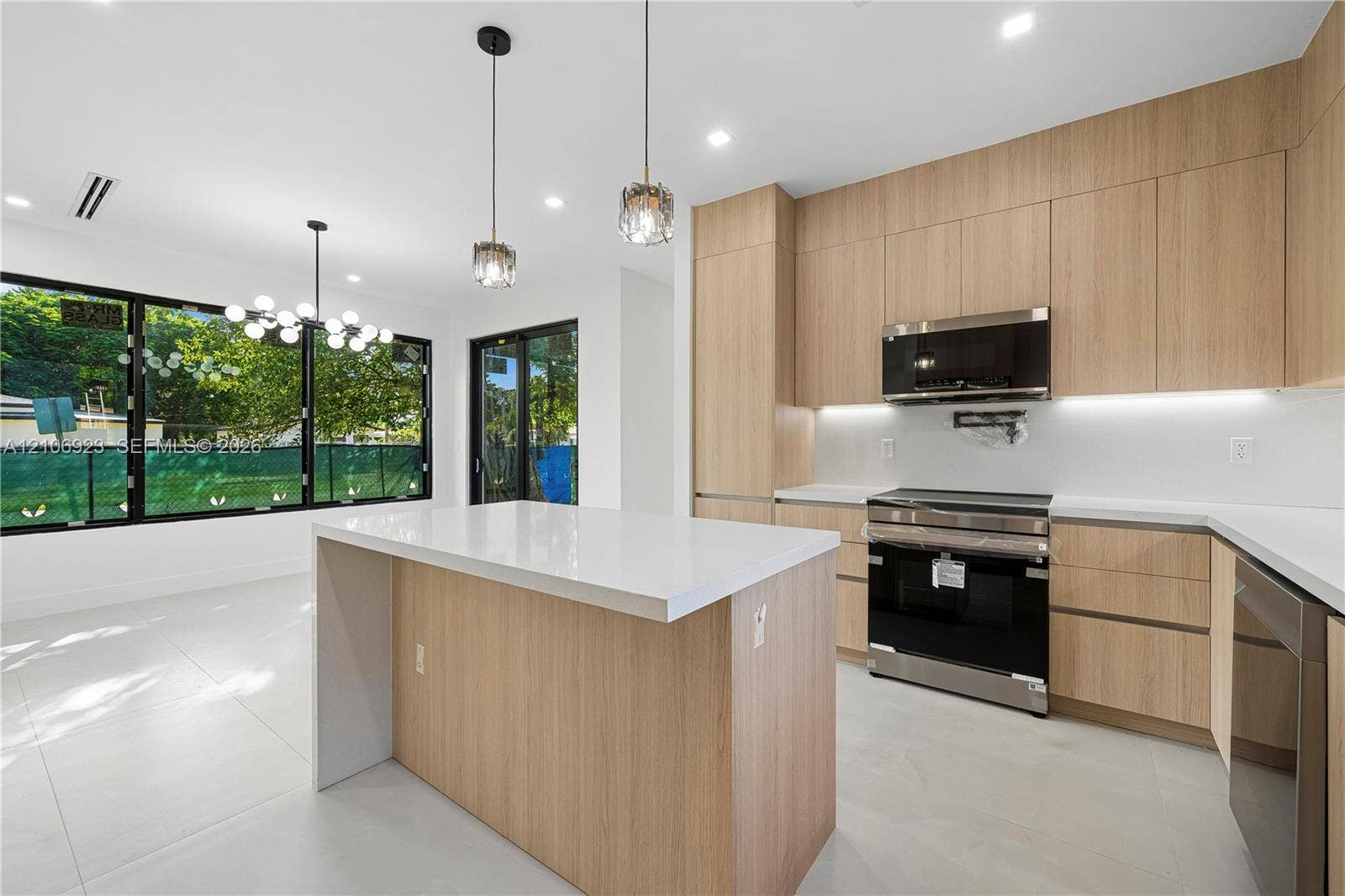 870 Superior Street, Opa Locka, FL 33054 Kitchen featuring light wood-finish cabinetry, a central island with a white countertop, large-format tile flooring, stainless steel appliances, and integrated under-cabinet lighting