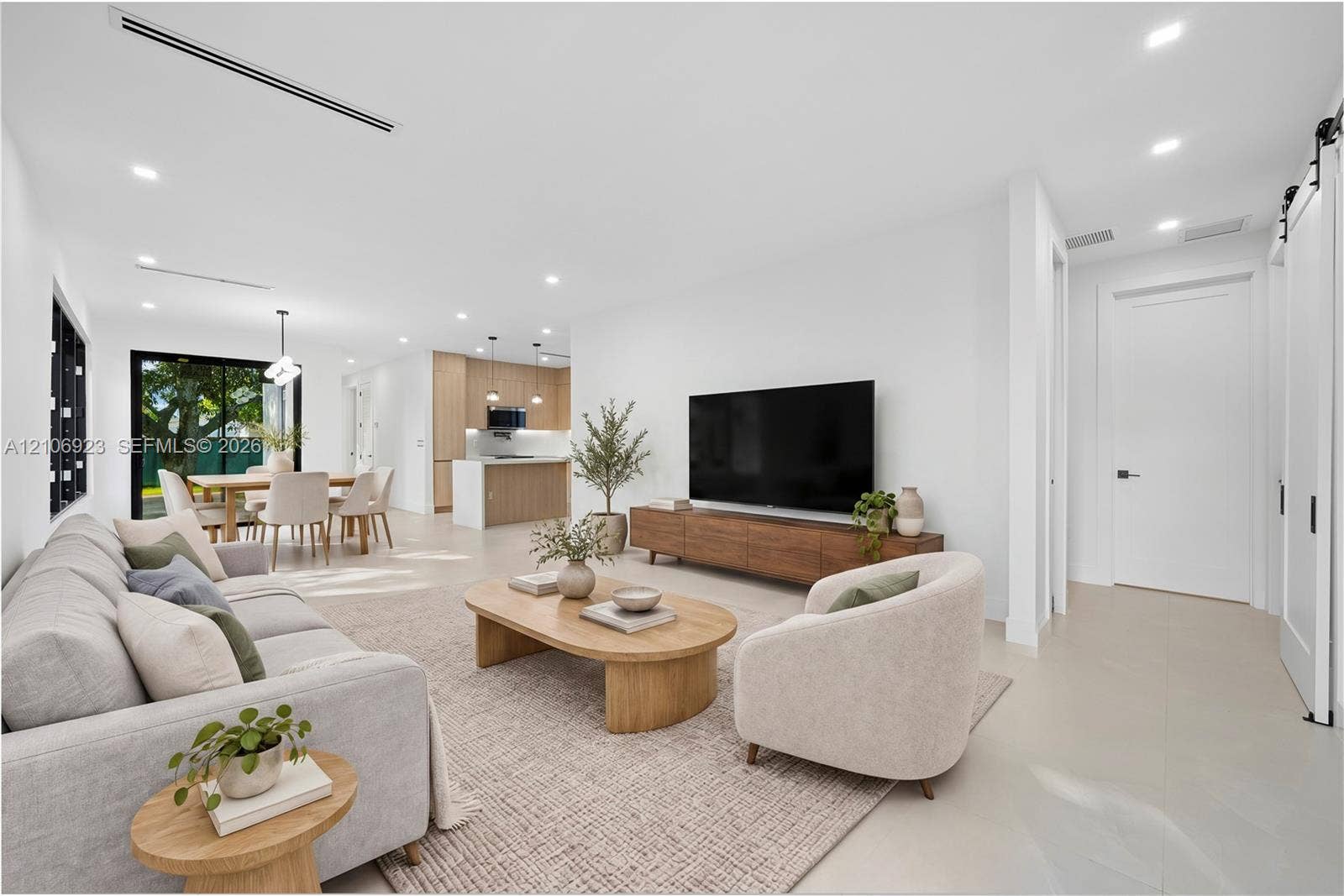 870 Superior Street, Opa Locka, FL 33054 Open-concept interior featuring light-toned flooring, recessed lighting, linear HVAC diffusers, white sliding barn door, and kitchen cabinetry with wood-finish accents