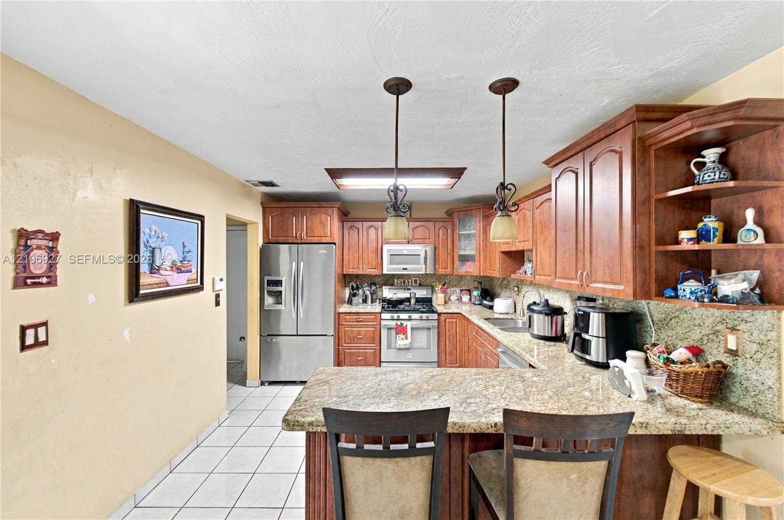 Kitchen featuring wood cabinetry, stone countertops, stainless steel appliances, tile flooring, and pendant lighting