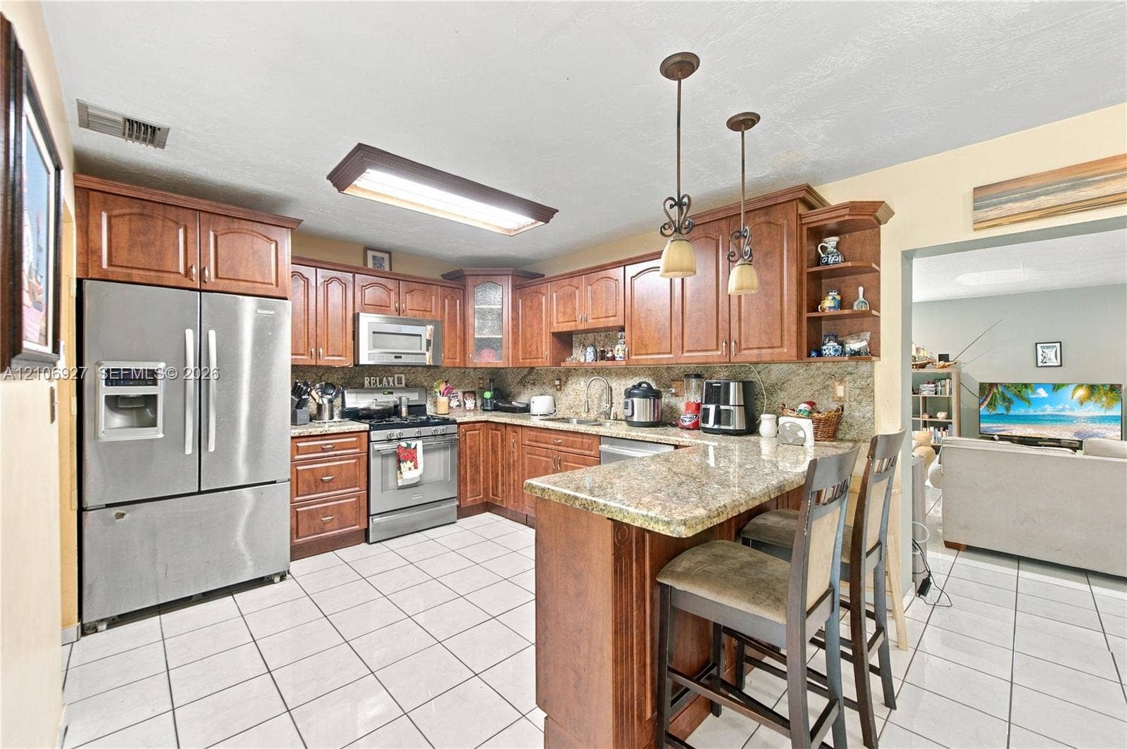 Kitchen featuring wood cabinetry, stone countertops, stainless steel appliances, ceramic tile flooring, and dual hanging pendant lights