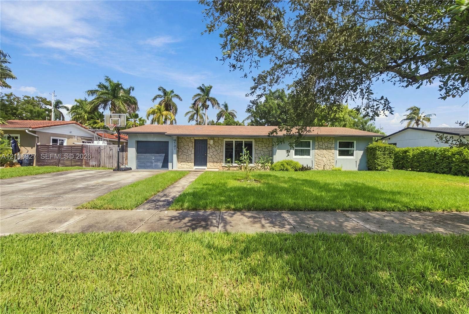 Single-story exterior featuring stone veneer accents, a low-slope roofline, concrete driveway, and a front lawn with mature landscaping